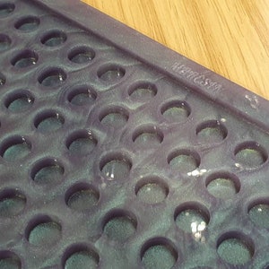 Puede incluir: Primer plano de un molde de resina morado y verde con una cuadrícula de hendiduras circulares. El molde tiene el texto "RESIN SUPPLY" en relieve en el lateral.