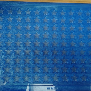 May include: A blue plastic mat with a pattern of stars embossed on the surface. The mat has a white border and the text "Safe Treads" is printed in the bottom right corner.