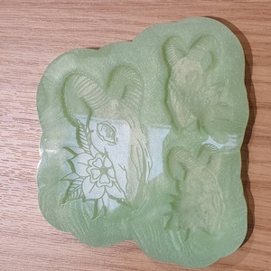 Peut inclure: Un moule en silicone vert clair représentant un crâne de bélier avec un motif floral. Le moule a une surface détaillée et texturée et est conçu pour le bricolage. Le crâne de bélier est centré avec des cornes incurvées.