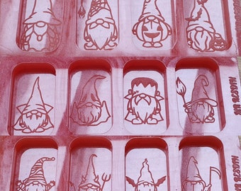 Könnte beinhalten: Eine rote Silikonform mit 10 einzelnen Vertiefungen in Form von Gnomen. Jeder Gnom hat ein anderes Design, darunter ein Kürbis, ein Hexenhut und ein Zuckerrohr.