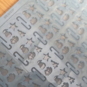 May include: A clear plastic sheet with a repeating pattern of Christmas-themed cutouts. The cutouts include stars, Christmas trees, candy canes, and gift boxes.