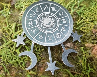 May include: A silver necklace with a circular pendant featuring the zodiac signs and a crescent moon. The pendant is attached to a black cord and has five dangling charms: three crescent moons and two stars.