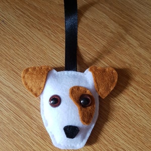 May include: A felt dog decoration with a black ribbon. The dog has brown ears and patches, with large, round, brown eyes. The dog's face is white, and it has a black nose. A charming handmade item.