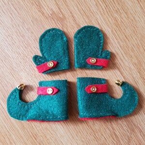 May include: Four felt elf shoes with red trim and gold buttons. The shoes are green and have pointed toes.