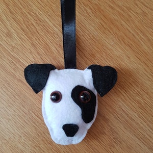 May include: A white and black felt dog ornament with black button eyes. The ornament has a black ribbon for hanging.