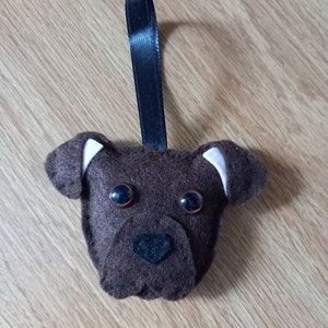 May include: Brown felt dog ornament with black eyes and a black nose. The ornament has a black ribbon loop for hanging.