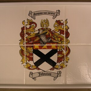 Puede incluir: Bandeja blanca para servir con un inserto de azulejo decorativo con un escudo familiar. El escudo incluye un yelmo, un pergamino y el nombre "Johnston". La bandeja tiene asas integradas.