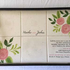 Puede incluir: Una bandeja rectangular con marco y asas negras. La bandeja presenta seis baldosas de color crema, decoradas con rosas rosas y hojas verdes. El texto "Heather and Joshua" está escrito en las baldosas, junto con los detalles de la boda.