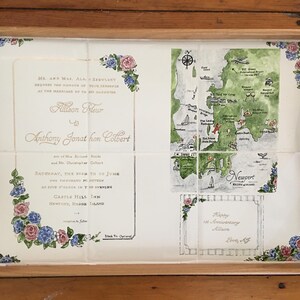 Puede incluir: Bandeja de madera con dise&ntilde;o floral y mapa. La bandeja presenta una invitaci&oacute;n de boda y un mapa de Newport, Rhode Island. La invitaci&oacute;n incluye los nombres Allison y Anthony, y la fecha de la boda.