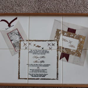 Puede incluir: Bandeja decorativa con marco y asas de madera. La superficie de baldosas blancas presenta dise&ntilde;os tem&aacute;ticos de boda, incluyendo invitaciones y una tarjeta "Save the Date". El dise&ntilde;o incluye detalles en color burdeos.