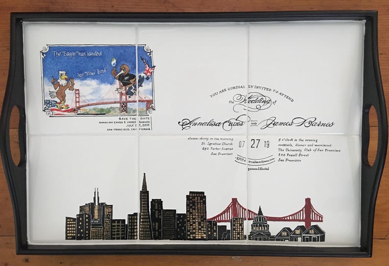 Puede incluir: Bandeja negra con una inserci&oacute;n blanca con el horizonte de San Francisco y detalles de boda. La inserci&oacute;n incluye ilustraciones del Golden Gate Bridge y personajes de dibujos animados. El texto incluye nombres, fecha y lugares.