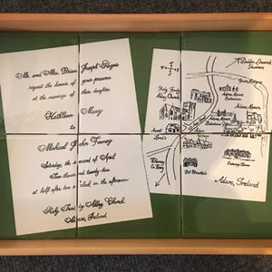 Puede incluir: Una bandeja de madera con una inserci&oacute;n de azulejos verdes, que contiene cuatro azulejos blancos con texto manuscrito negro. Los azulejos muestran detalles de boda, incluyendo un mapa y nombres.