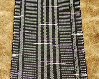 Black rag rug with dashes of purple, green and tan cotton fabric. 79x24 inches