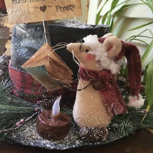May include: A whimsical Christmas decoration featuring a mouse wearing a Santa hat and scarf, with a small candle and a sign that reads "I'll be back again some day" Frosty. The mouse is tan with pink ears and a red scarf.