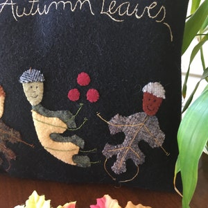 May include: A navy blue pillow with the embroidered text "Autumn Leaves". The pillow features appliqued leaf and acorn designs in various colors. Decorative fall-themed pillow.