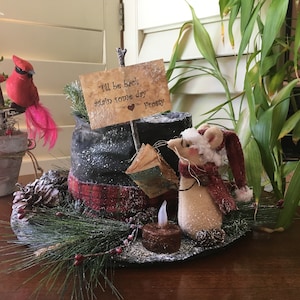 May include: A festive holiday decoration featuring a red cardinal perched on a miniature Christmas tree, a snowman's hat, and a mouse wearing a Santa hat and scarf. The sign reads "I'll be back again some day Frosty."