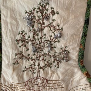 Puede incluir: Calcet&iacute;n navide&ntilde;o color crema con borde estampado en verde y dorado. El calcet&iacute;n presenta un dise&ntilde;o de &aacute;rbol de Navidad bordado adornado con abalorios plateados. El &aacute;rbol est&aacute; decorado con varios adornos, incluyendo un &aacute;ngel, un copo de nieve y un mu&ntilde;eco de nieve.