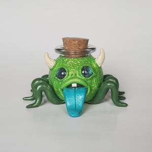 Pequeño tarro de monstruo, monstruo verde único en su tipo con lengua y cuernos verde azulado