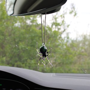 May include: A green and purple glass spider car charm hanging from the rearview mirror of a car.