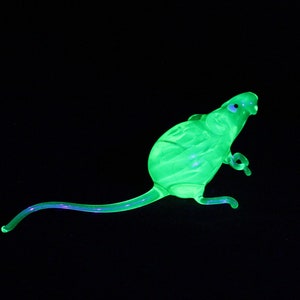 May include: A green glass figurine of a mouse with a long tail. The figurine is made of uranium glass and glows under a black light.
