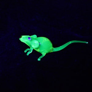 May include: A green glass mouse figurine with purple eyes. The figurine is glowing under a black light.