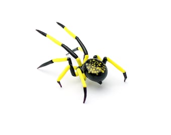 May include: A black and yellow glass spider figurine with a detailed black and gold patterned body.