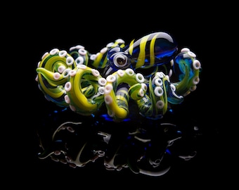 May include: A glass octopus sculpture with blue, yellow, and white swirls. The octopus has eight tentacles and large, white eyes.