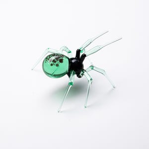 May include: A green glass spider with black accents and a speckled abdomen.