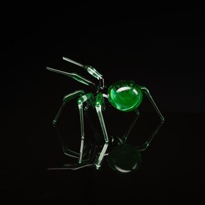 May include: A green glass spider sculpture with a round, green glass body and eight long, thin legs. The spider is sitting on a black surface.