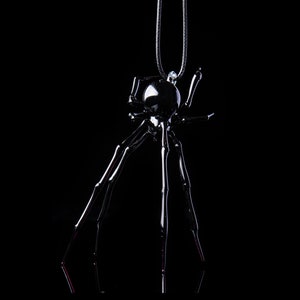 May include: A black metal spider pendant necklace with a shiny finish. The spider has eight long legs and a round body.
