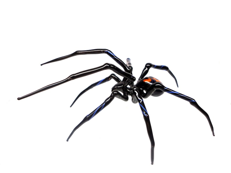 Puede incluir: Una escultura de ara&ntilde;a de vidrio negro con detalles azules y un abdomen naranja. La ara&ntilde;a tiene ocho patas y est&aacute; en posici&oacute;n de arrastre.