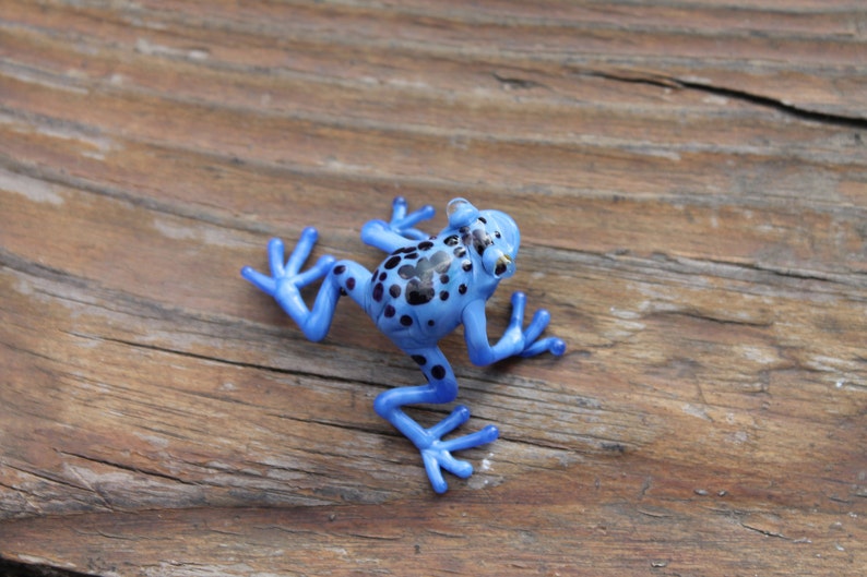 May include: A blue and black glass frog figurine with a spotted pattern. The frog is posed with its legs outstretched and its head tilted slightly to the side.