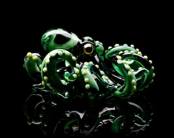 May include: A green glass octopus sculpture with yellow accents. The octopus has eight tentacles and is curled up in a ball.