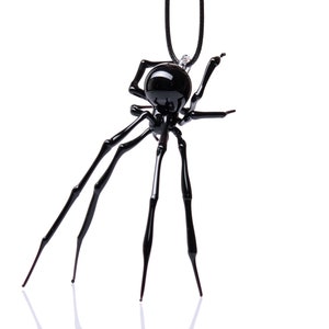 May include: A black glass spider pendant necklace. The spider has eight legs and a round body. The necklace is hanging from a black cord.
