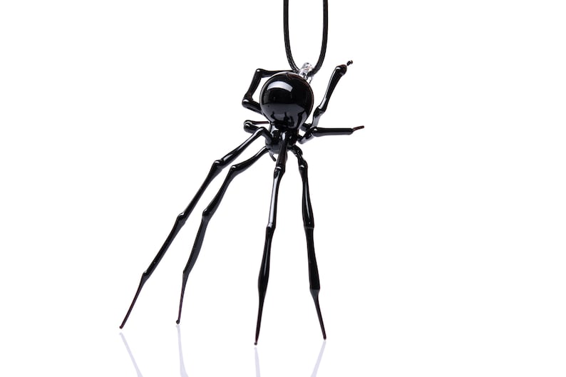 May include: A black glass spider pendant necklace. The spider has eight legs and a round body. The necklace is hanging from a black cord.