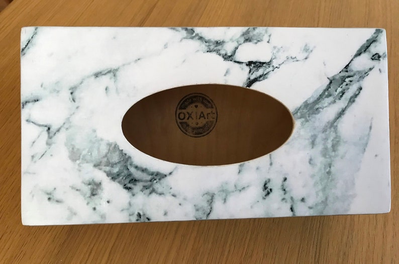 May include: White marble tissue box cover with a rectangular opening for tissues. The cover has a wood-like interior with a black and white logo that says "OXIA&reg;".