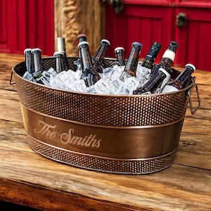 May include: A copper-colored metal ice bucket with a hammered finish and a personalized inscription that reads "The Smiths". The bucket is filled with ice and bottles of beer.
