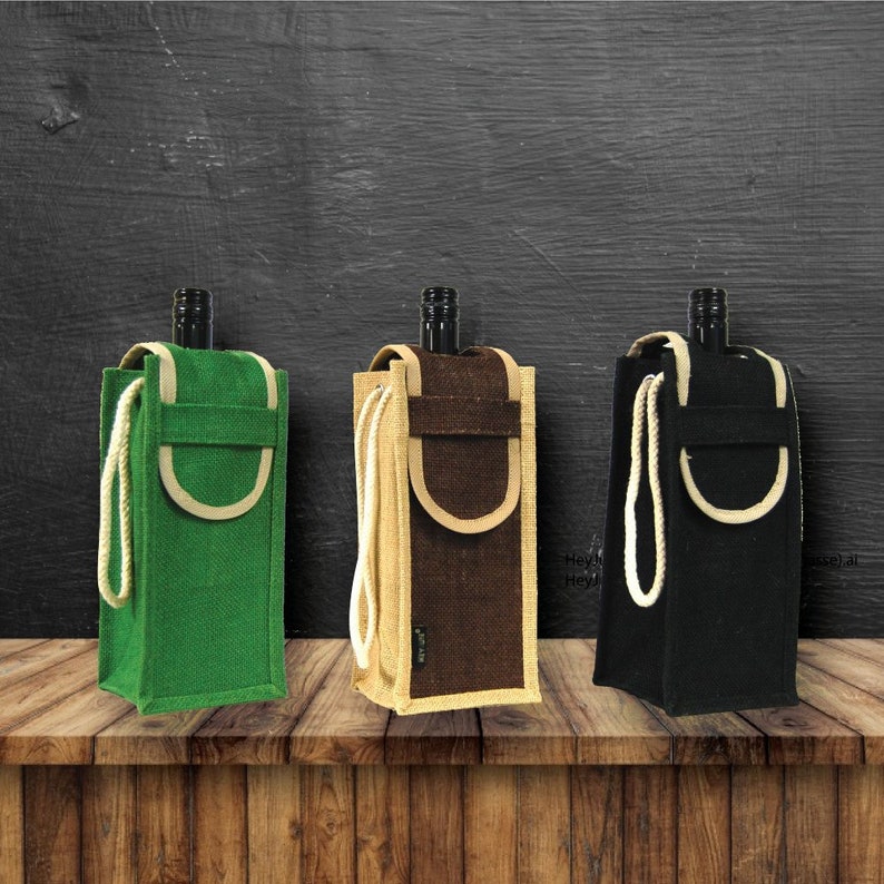 May include: Three reusable wine bottle bags made of natural jute fabric. The bags are in green, brown, and black colors. Each bag has a white rope handle and a cream-colored flap with a pocket.