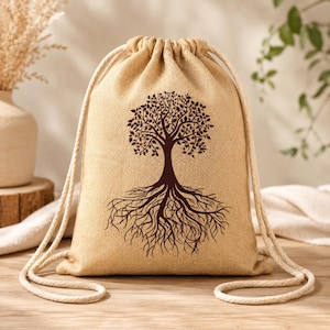 Puede incluir: Una bolsa beige con cordón y un diseño de árbol marrón oscuro. El árbol presenta un tronco, ramas y raíces detallados. La bolsa tiene un aspecto texturizado y está hecha de una tela de aspecto natural. Se ven cordones blancos en forma de cuerda.