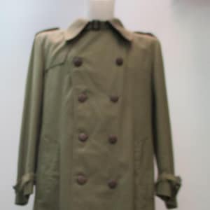 May include: A khaki-colored trench coat with a double-breasted design. The coat features a notched collar, epaulets, and a belt detail at the cuffs. It has large, dark brown buttons and a knee-length hemline, offering a classic, timeless look.