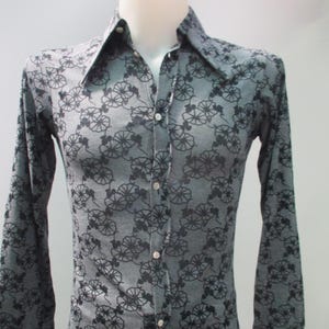 May include: A gray long-sleeve button-down shirt with a black floral pattern. The shirt has a pointed collar and is buttoned up. The floral design is repeated across the fabric.