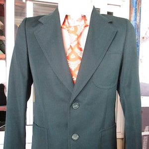 May include: A dark green blazer with two button fastenings and two flap pockets. The blazer has a white shirt and an orange patterned tie underneath.