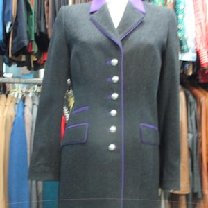 May include: A dark gray blazer with a purple collar and trim, displayed on a mannequin. The blazer has silver buttons and two front pockets with purple trim. The clothing item is part of a collection of garments.