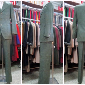 May include: A green tweed suit jacket and trousers on a mannequin. The jacket has a notched lapel and three buttons. The trousers have a straight leg.