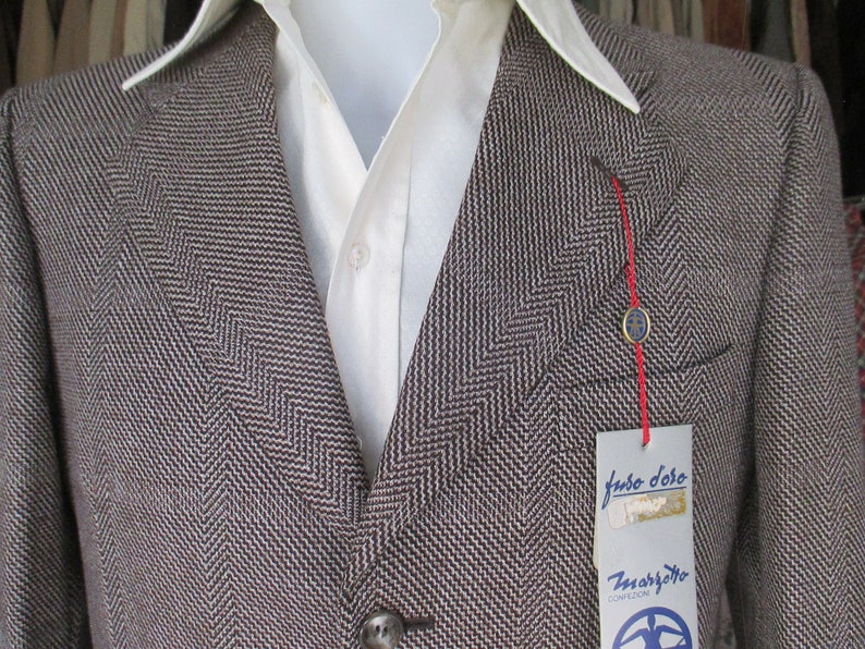 May include: A brown and white herringbone blazer with a red string and a tag that reads "Judo Doro" and "Zmargotto Confezioni".