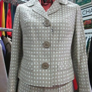 May include: A beige blazer and skirt set with white polka dots. The blazer has a notched collar and three buttons down the front. The skirt is a-line and has pleats.