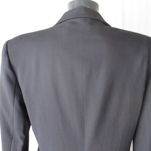 May include: A black blazer with a notched lapel, displayed on a mannequin. The back view shows the tailored fit and the smooth texture of the fabric. The blazer has a classic, professional design.