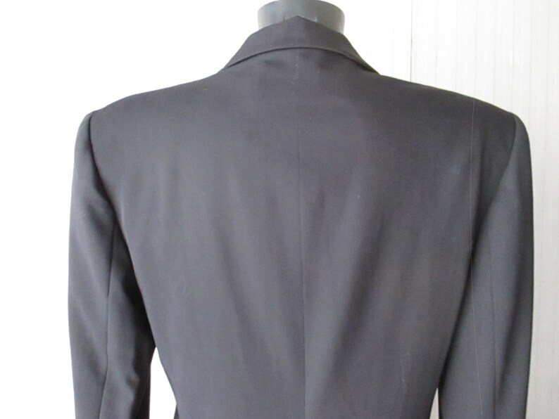 May include: A black blazer with a notched lapel, displayed on a mannequin. The back view shows the tailored fit and the smooth texture of the fabric. The blazer has a classic, professional design.