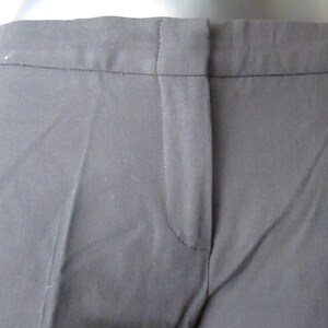 May include: Close-up of black dress pants. The pants have a tailored design with a button and zipper closure. The fabric appears to be a smooth, woven material. The pants are a solid black color.