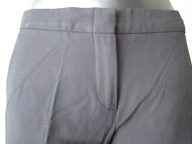 May include: Close-up of black dress pants. The pants have a tailored design with a button and zipper closure. The fabric appears to be a smooth, woven material. The pants are a solid black color.